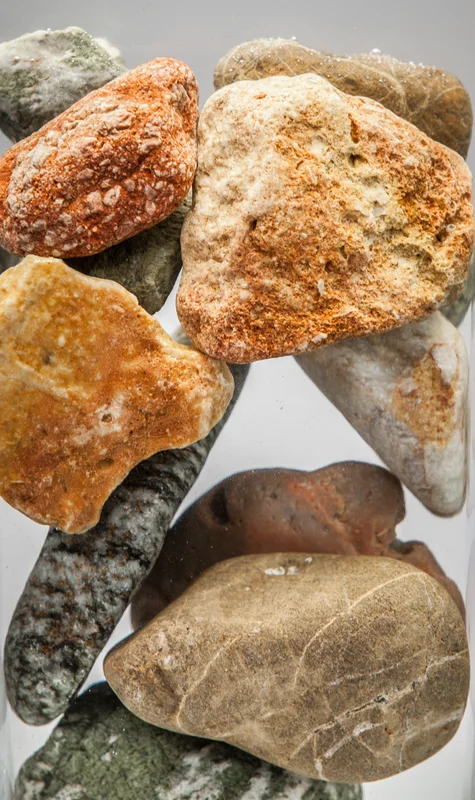 A close vertical arrangement of rounded stones in clear water or a transparent vessel.