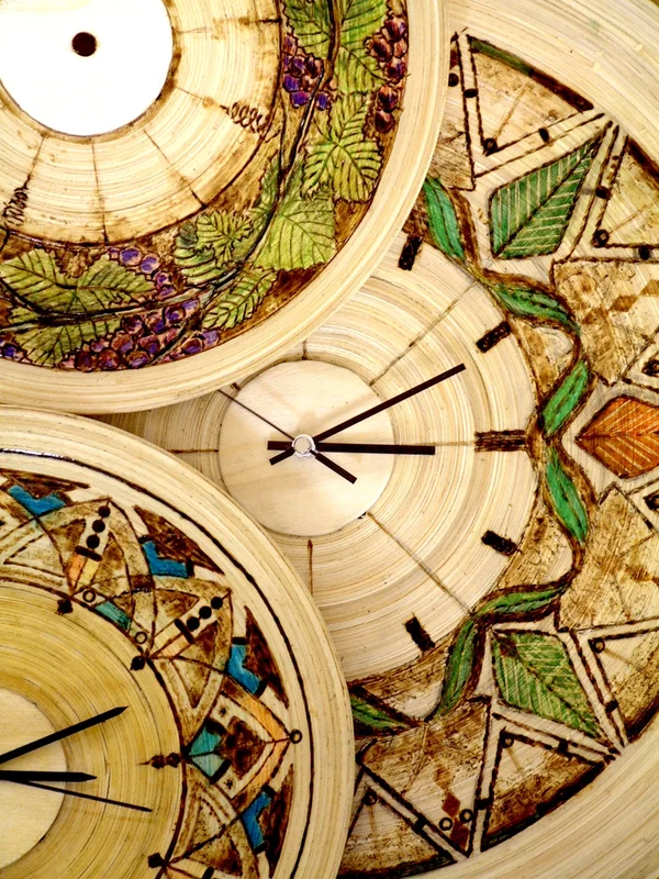 Overlapping round wooden clocks decorated with geometric, leaf and grape motifs.