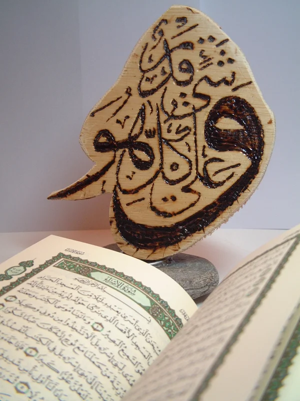 A freeform wood-grain calligraphic panel on a small base, with an open book in the foreground.